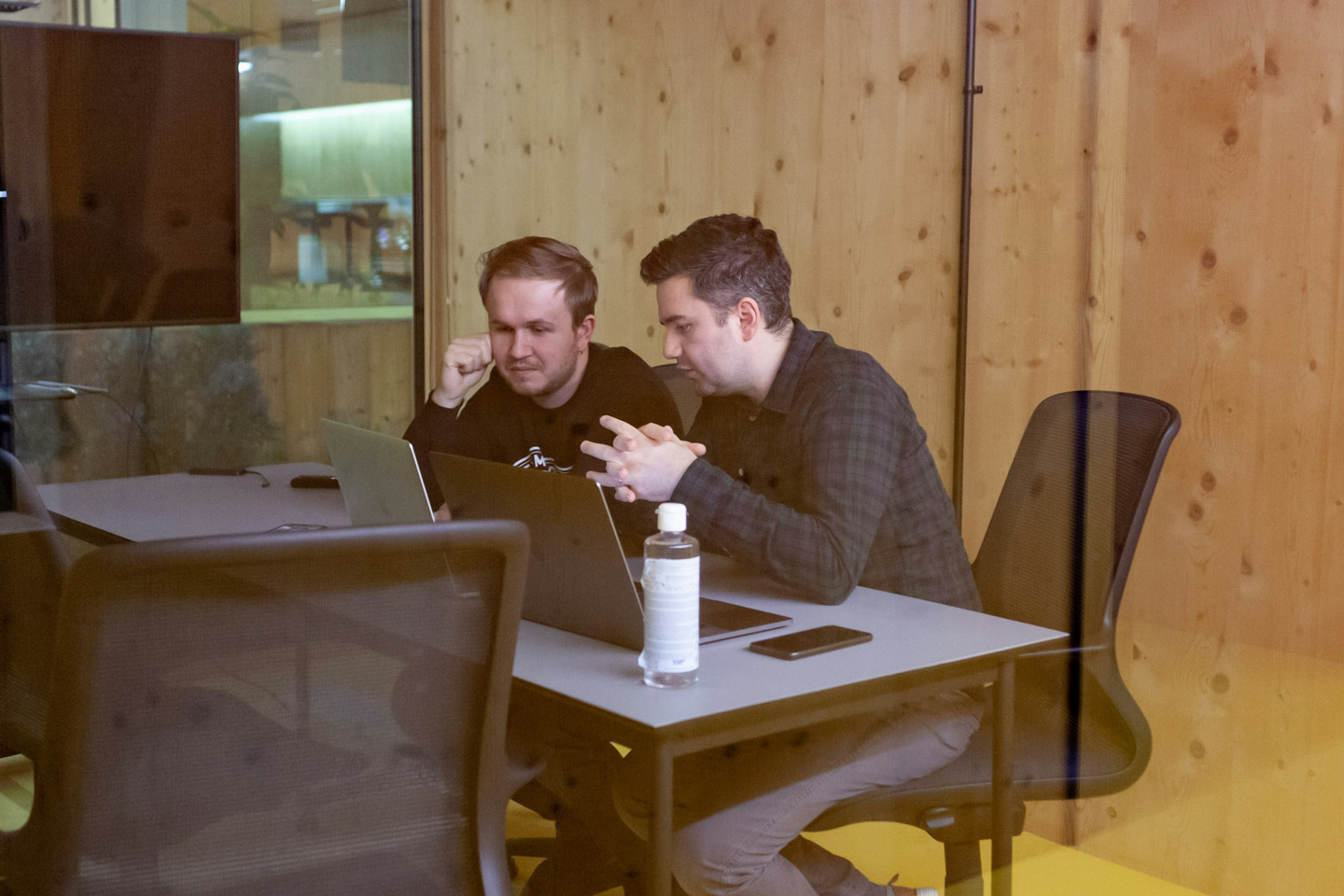 Two colleagues discussing work while looking at laptops together in a modern wood-panelled meeting room