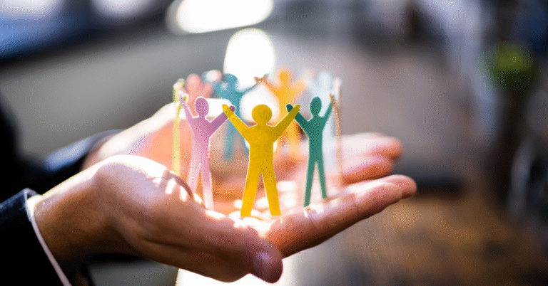 A person's hands cup a circle of colorful paper cutout figures holding hands, symbolizing teamwork, community, and support. This image represents the human element in future-proofing leadership.