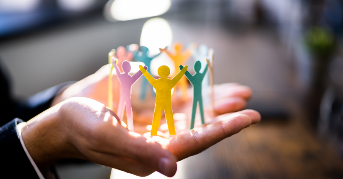 A person's hands cup a circle of colorful paper cutout figures holding hands, symbolizing teamwork, community, and support. This image represents the human element in future-proofing leadership.