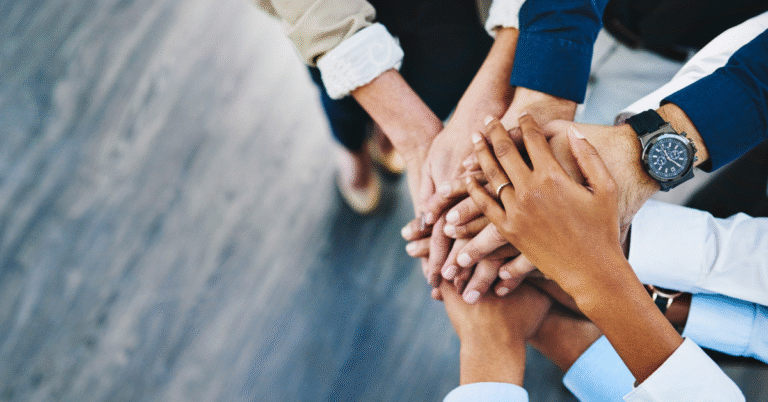 A diverse group of hands stacked together, symbolizing unity and teamwork, essential for strong leadership team collaboration.