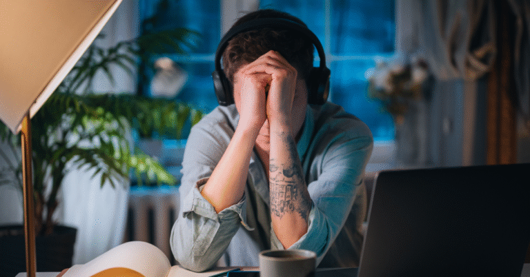 A stressed woman in a business setting covers her face with her hands, visually representing the struggle with impostor syndrome in a senior role.