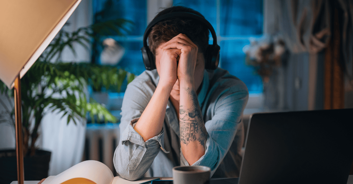 A stressed woman in a business setting covers her face with her hands, visually representing the struggle with impostor syndrome in a senior role.