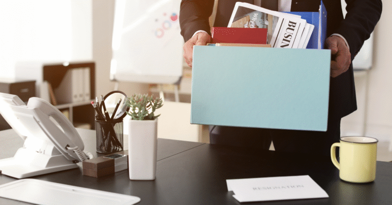 A business man is packing up his office desk and holding a box of his belongings representing Mistakes Companies Make During Redundancy